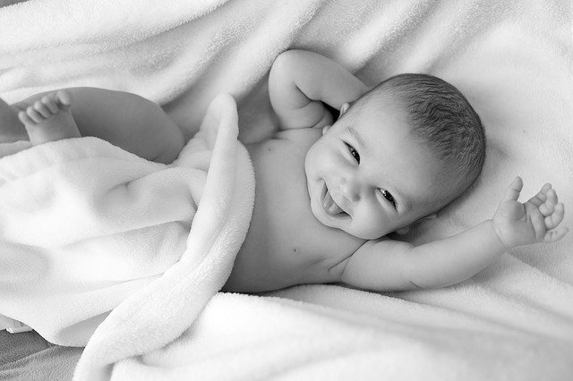 Bébé souriant déshabillé et emmitouflé dans une couverture chaude pendant une séance de massage bébé.