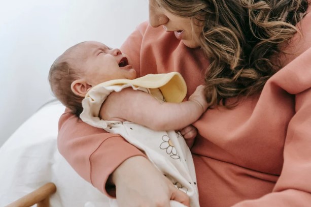 Bébé qui pleure dans les bras de sa maman.
